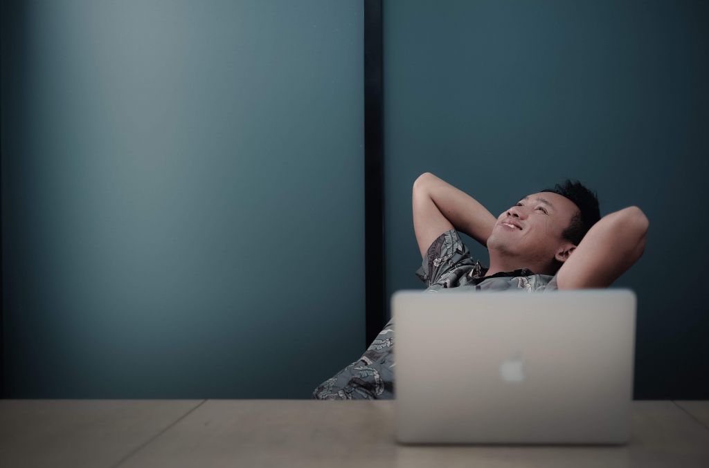 Homem sorrindo e relaxado em frente a um notebook.