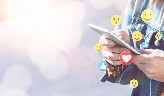 live shopping - imagem mostra as mãos de uma pessoa segurando um smartphone com ilustrações de emojis ao redor