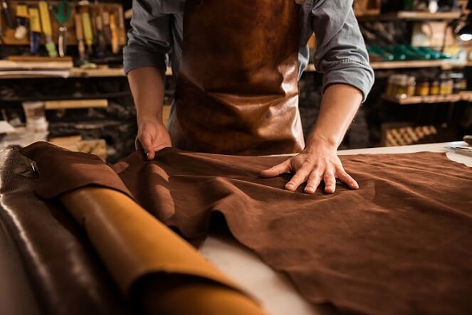 foto de produção de artesanato, com um homem trabalhando com tecidos e materiais em couro em um ateliê