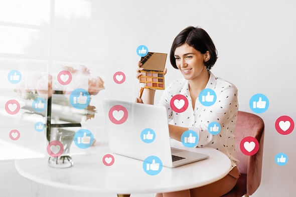mulher olha para um notebook, cercada de ícones de curti e amei em redes sociais
