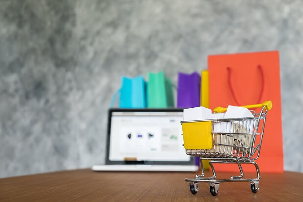 imagem de um notebook ao fundo, cerca por carrinho de compras e sacolas, simulando uma loja virtual