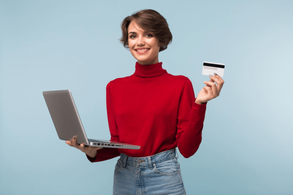 Mulher de camisa vermelha sorrindo. segurando um laptop e um cartão de crédito