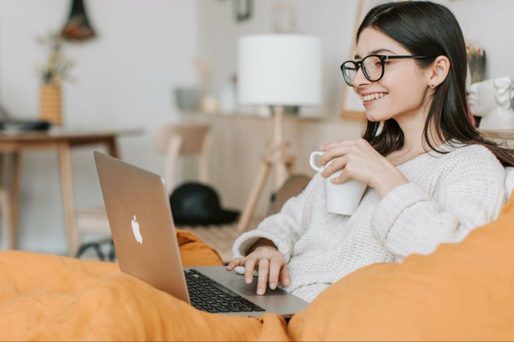 Mulher de óculos segurando uma caneca e utilizando laptop