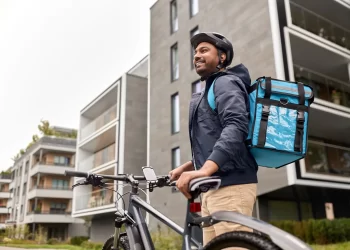 Entregador Loggi realizando coleta domiciliar com bicicleta em frente a edifícios residenciais — serviço de coleta domiciliar Loggi via Melhor Envio.