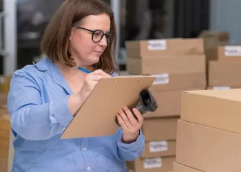 Profissional conferindo caixas com prancheta e leitor de código de barras, representando o uso do Loggi rastreamento no controle de encomendas