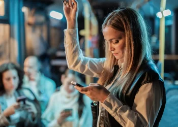 Mulher usando o celular em transporte público, ilustrando o uso de modelo de mensagem automática para atendimento pelo WhatsApp.