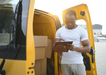 Entregador conferindo lista de envios ao lado de van amarela, representando o uso de plataformas de frete para e-commerce