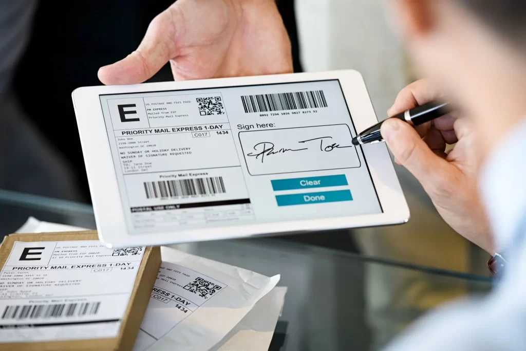 Etiqueta de envio Correios sendo assinada digitalmente em tablet, com pacotes prontos para envio.