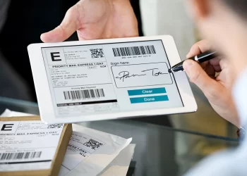 Etiqueta de envio Correios sendo assinada digitalmente em tablet, com pacotes prontos para envio.