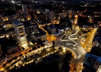 Vista aérea noturna da cidade de Cuiabá com iluminação urbana, edifícios modernos e tráfego intenso em avenidas movimentadas.