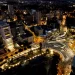 Vista aérea noturna da cidade de Cuiabá com iluminação urbana, edifícios modernos e tráfego intenso em avenidas movimentadas.