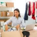 Lojista organizando estoque com peças recebidas de fornecedores de roupas, em ambiente de loja virtual com araras e caixas para envio
