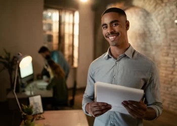 Empreendedor sorridente segurando documentos sobre tipos de empresas em ambiente corporativo, avaliando estrutura ideal para abrir um negócio.