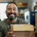 Empreendedor sorrindo enquanto prepara encomenda, representando o conceito de overdelivery no e-commerce