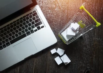 Laptop ao lado de um mini carrinho de compras com caixas