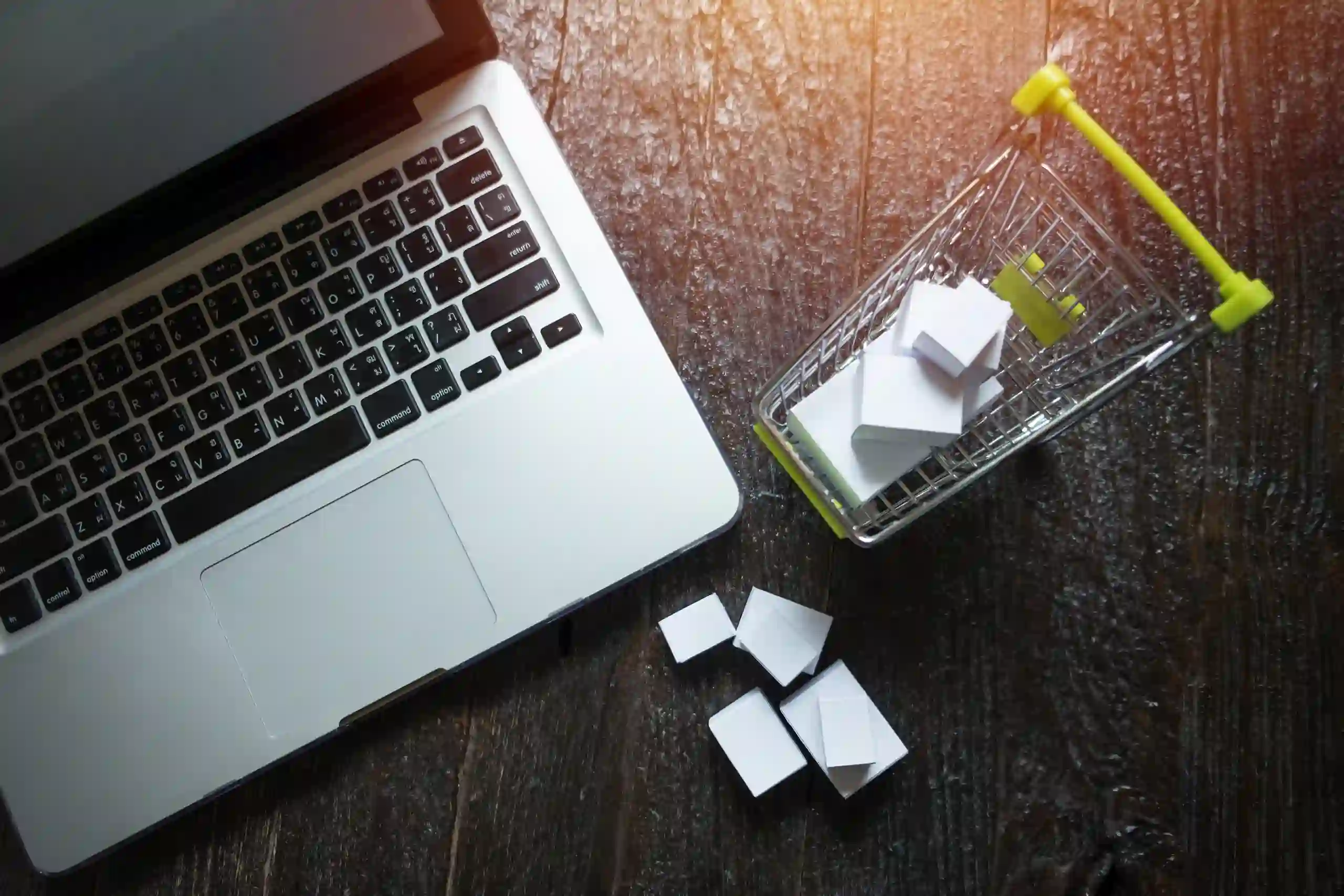 Laptop ao lado de um mini carrinho de compras com caixas